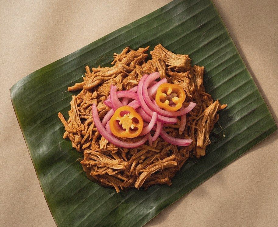 Shredded cochinita pibil on a banana leaf, topped with pickled red onion and habanero